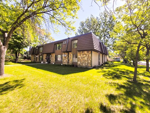 A house with a brown roof is surrounded by green grass and trees.