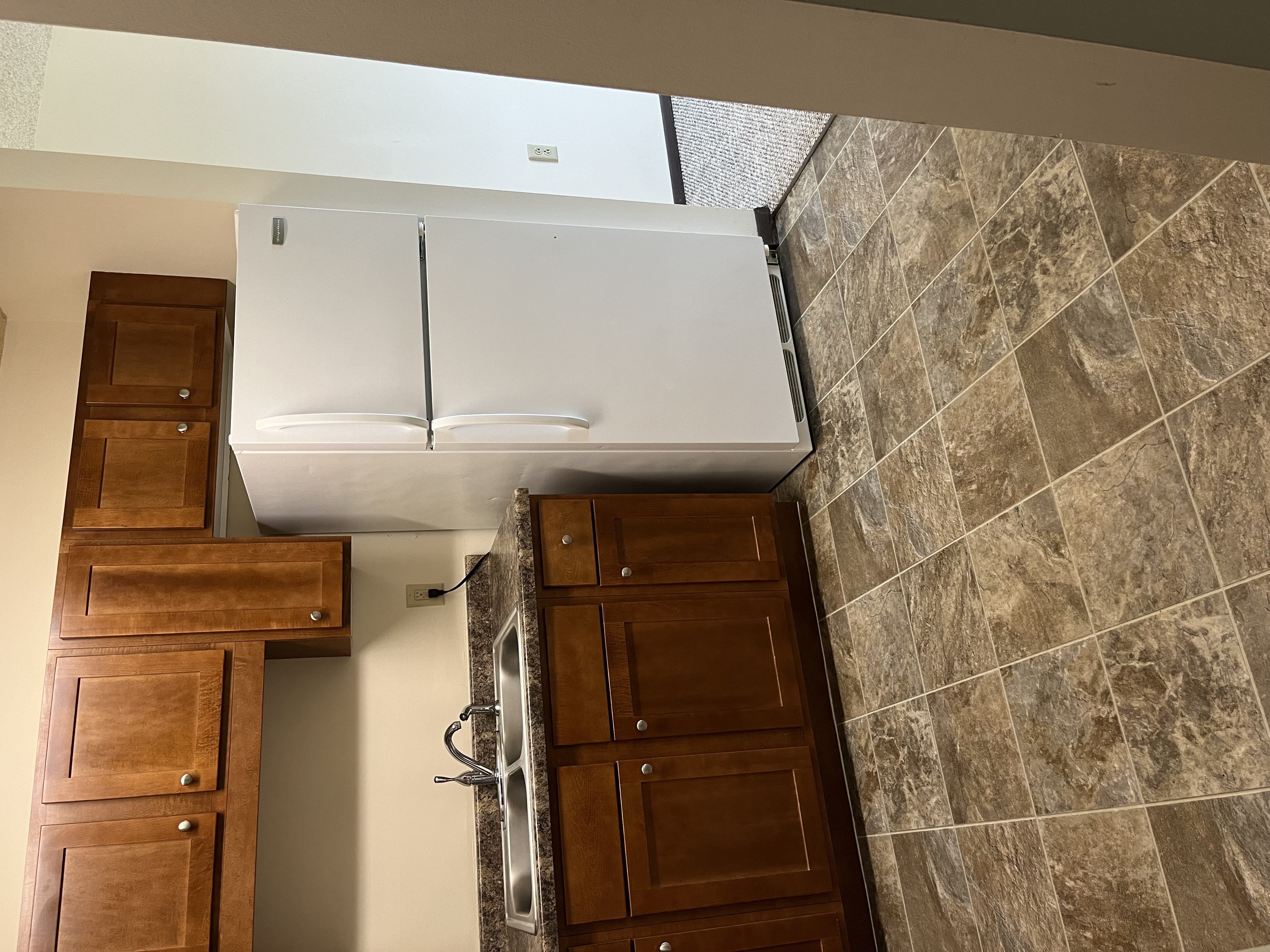 A white refrigerator is installed in a kitchen with brown cabinets.