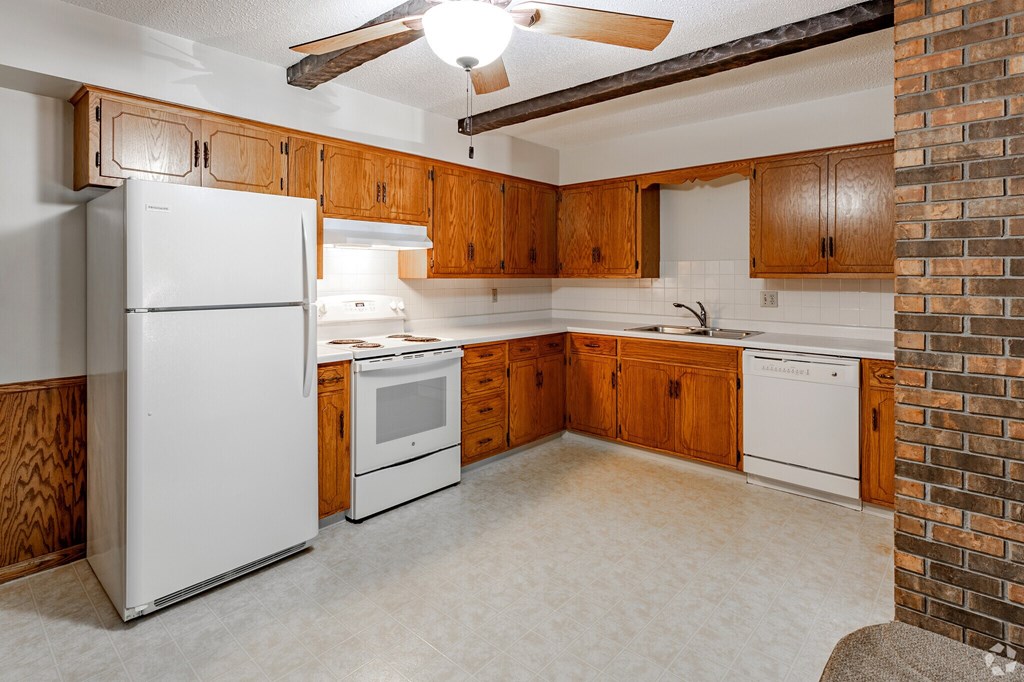 A kitchen with a white refrigerator, wooden cabinets, and a brick wall.