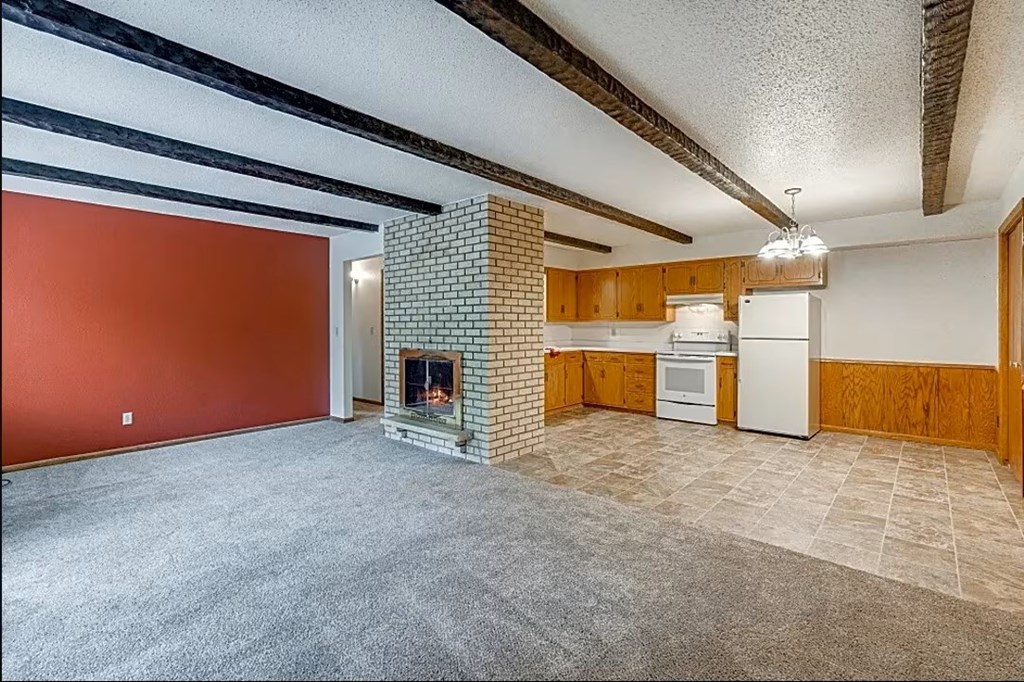 A living room with a fireplace and a kitchen area in the background.