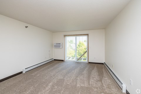 A spacious room with a carpeted floor and a sliding glass door leading to a balcony.