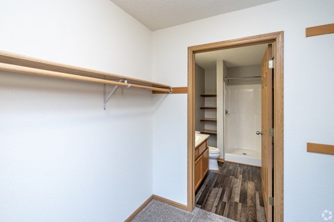 A white wall with a wooden shelf and a doorway leading to a bathroom.