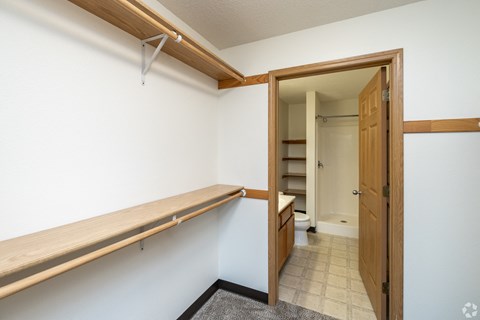A white wall with a brown shelf and a doorway leading to a bathroom.