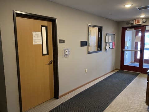 A hallway with a door on the left and a red door on the right.