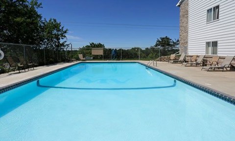 A rectangular blue swimming pool with a white fence and a house in the background.