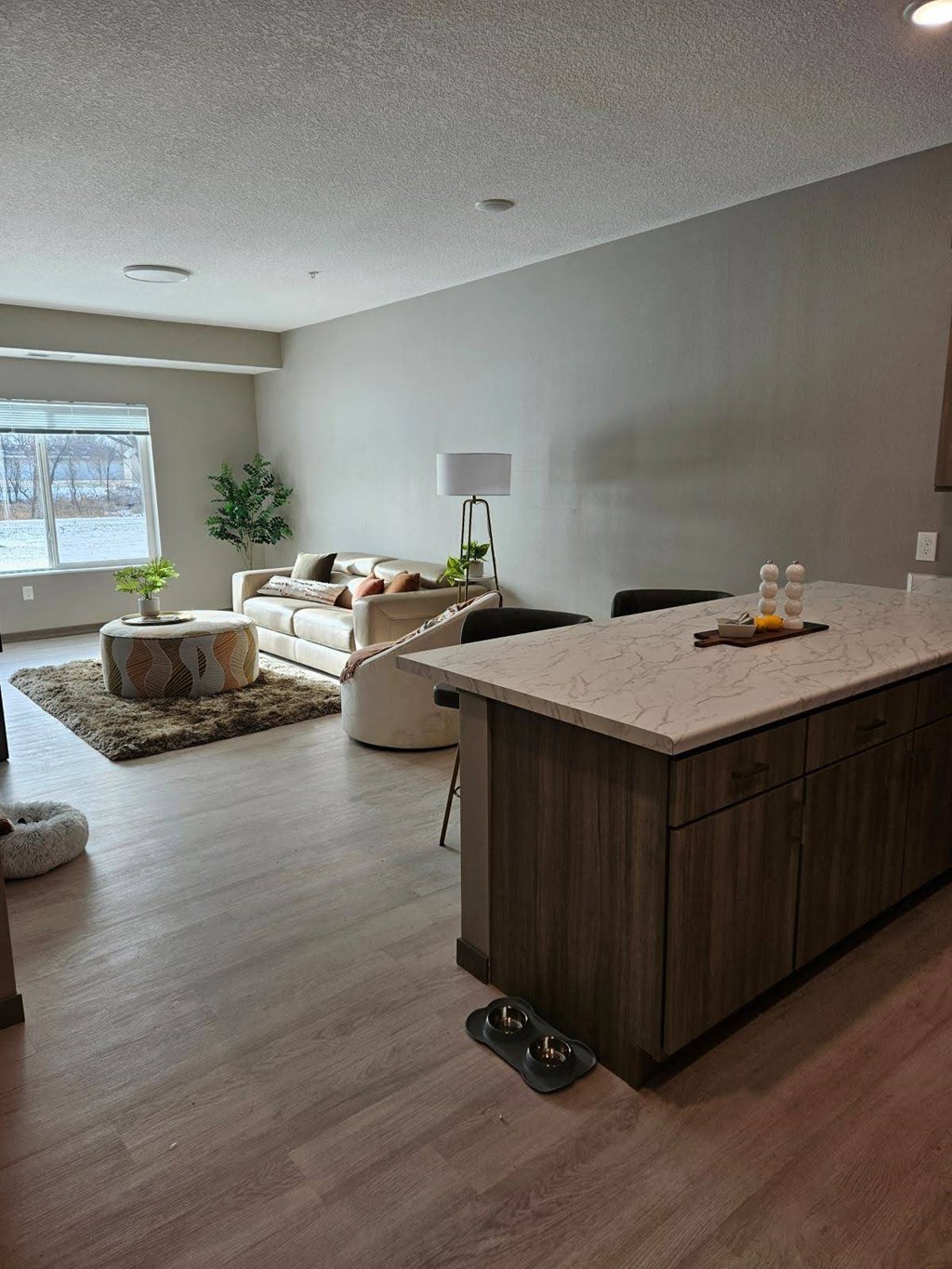A kitchen island with a marble top is in the middle of a room with a couch, chairs, and a potted plant.