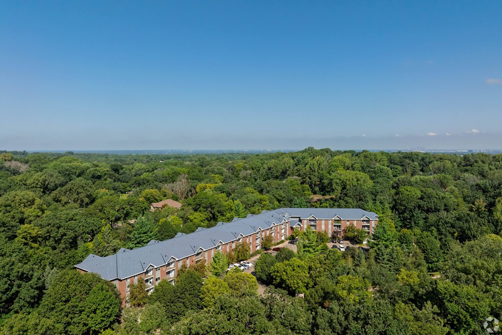 A large building with a grey roof is surrounded by green trees.