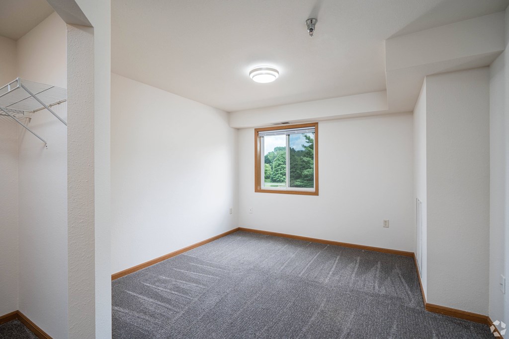 A room with a window and a grey carpet.