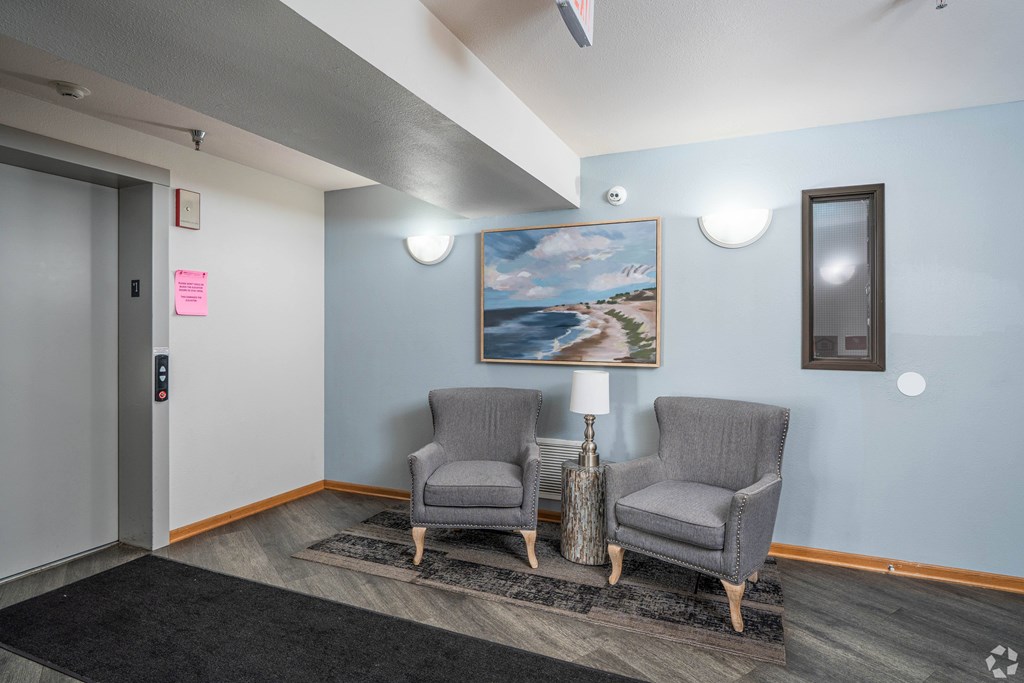 Two grey chairs are placed in front of a painting in a room.