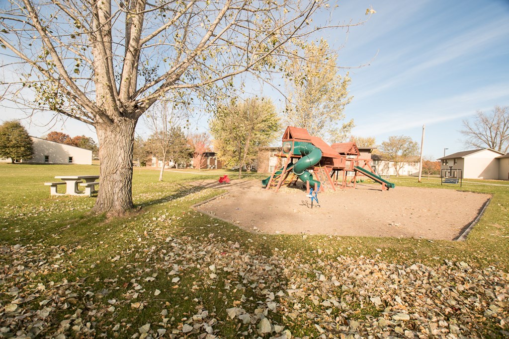 A playground with a green slide and a red building in the background.