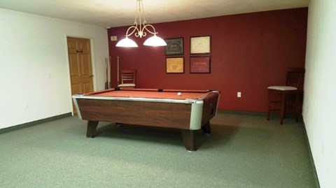 A room with a pool table and a green carpet.