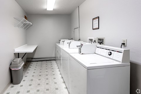 A laundry room with a washer and dryer, a trash can, and a white counter.