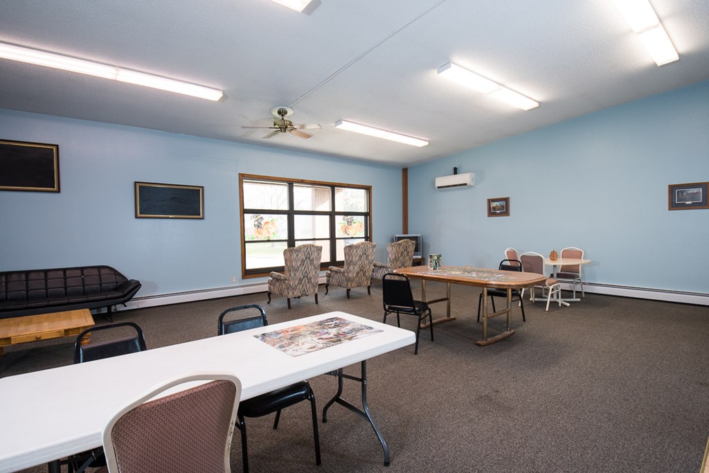 A room with a white table and chairs, a ceiling fan, and a window with a view of trees.