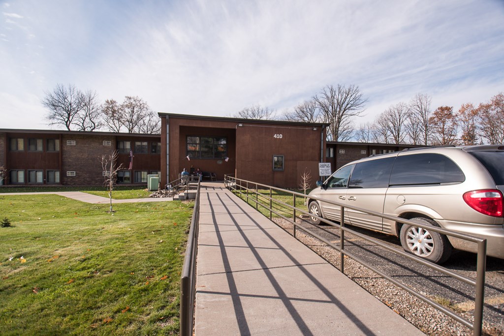 A silver car is parked on the side of a road in front of a brick building.