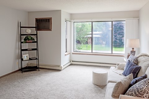 A living room with a white couch and a window overlooking a green area.