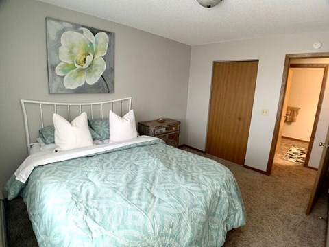 A bedroom with a bed, nightstand, and a painting of a flower on the wall.