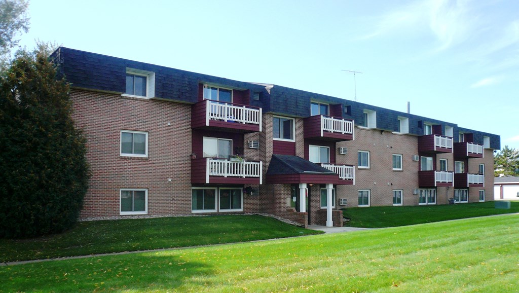 A red brick building with white balconies and a green lawn in front.
