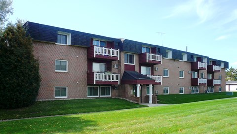 A red brick building with white balconies and a green lawn in front.