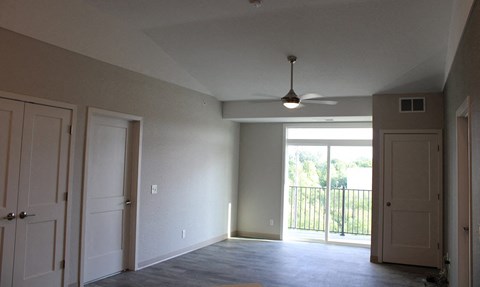 an empty living room with a ceiling fan and a balcony