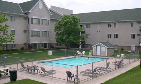 A pool surrounded by chairs and apartment buildings.