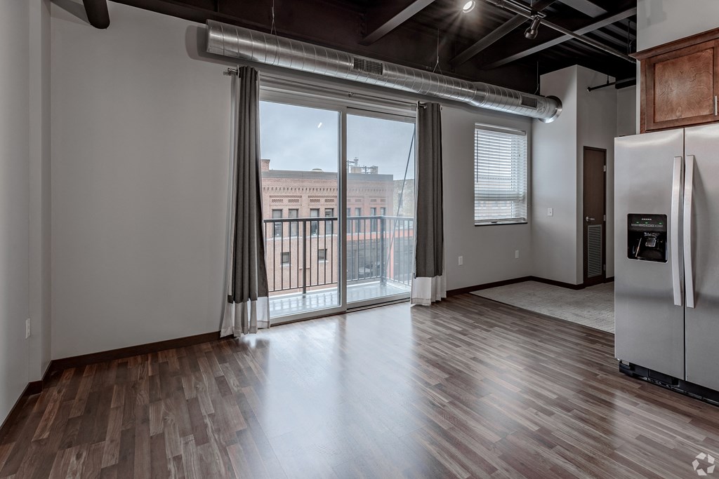 an empty living room with a large window and a door to a balcony