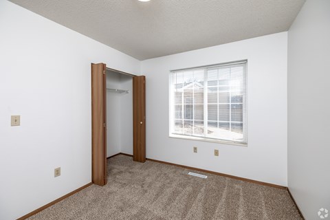 A room with a carpeted floor, a window with blinds, and a door.