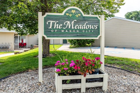 A sign that says "The Meadows of Mason City" with flowers in a planter box.