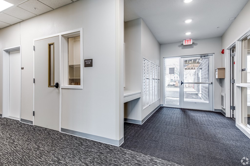 A hallway with a carpeted floor, white walls, and a door with a glass window.