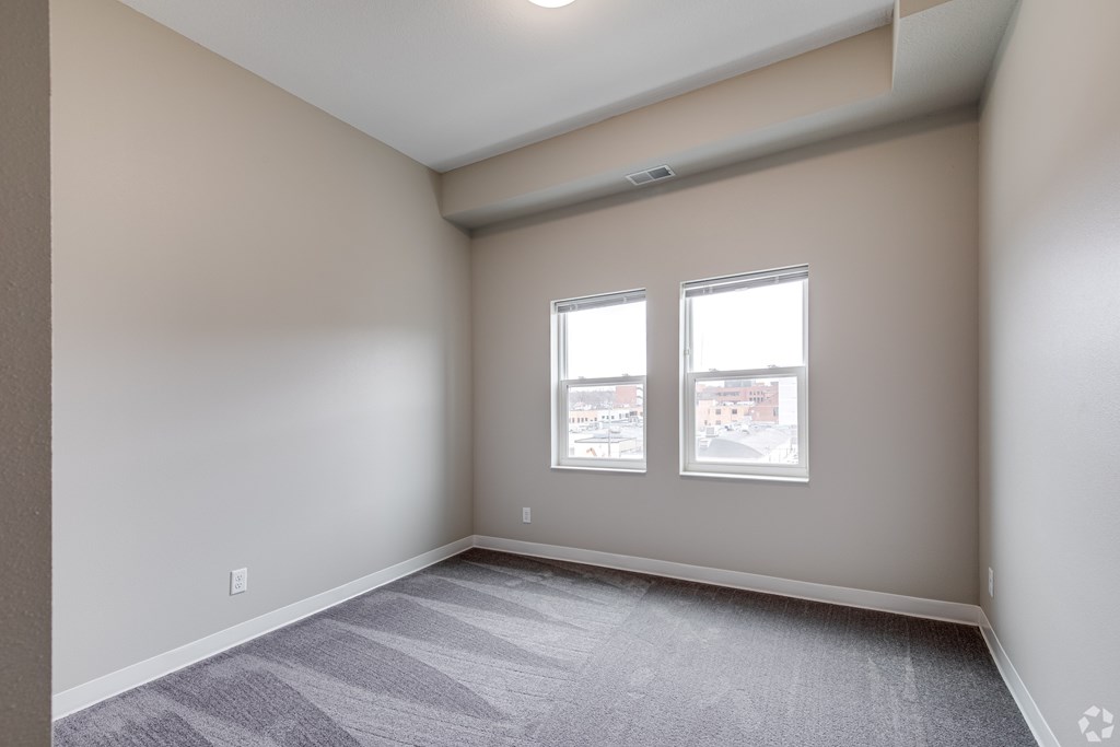 A room with a carpeted floor and two windows.