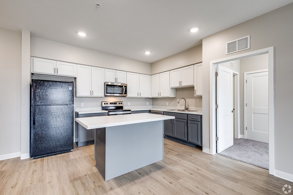 A kitchen with a black fridge and a white island.
