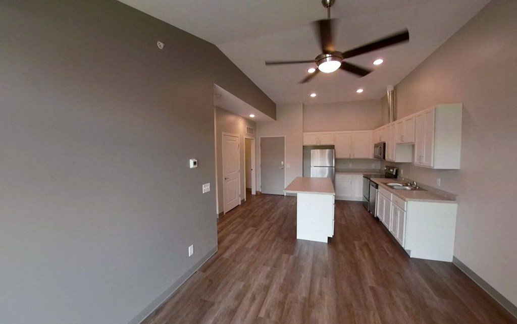 an empty living room and kitchen with a ceiling fan
