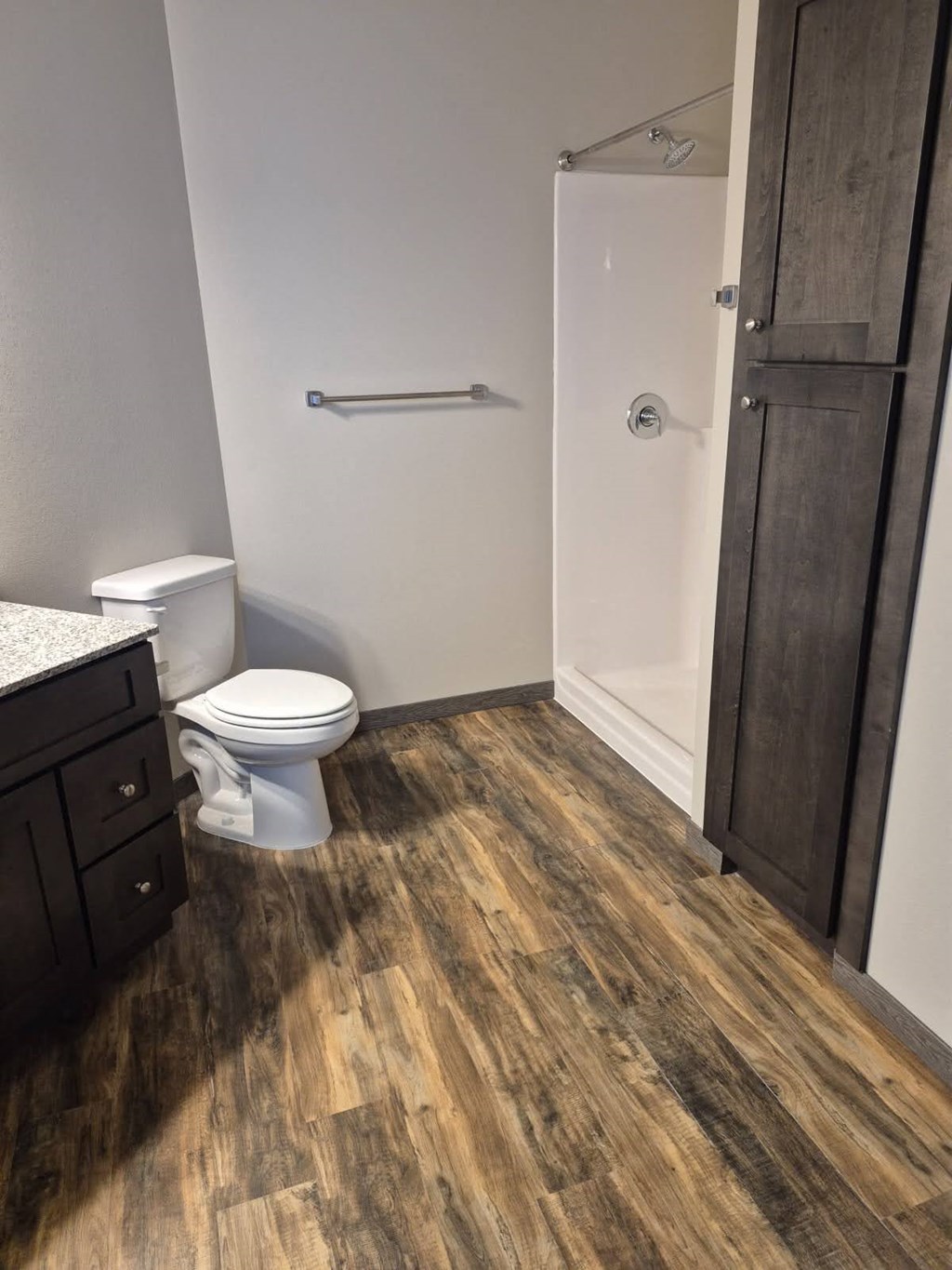 A white toilet sits next to a white sink in a bathroom with wood flooring.