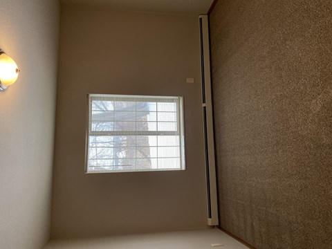 A window with blinds in a room with a light on the wall.