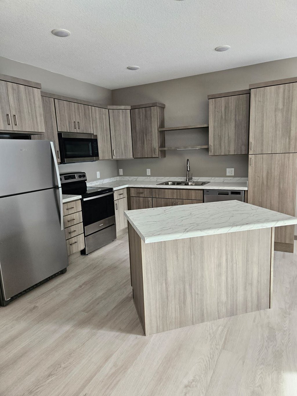A modern kitchen with a refrigerator, microwave, oven, sink, and cabinets.
