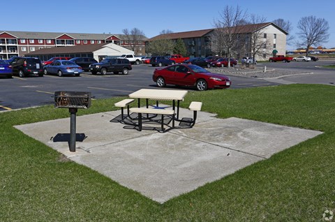 A picnic table sits in a concrete area in front of a parking lot.