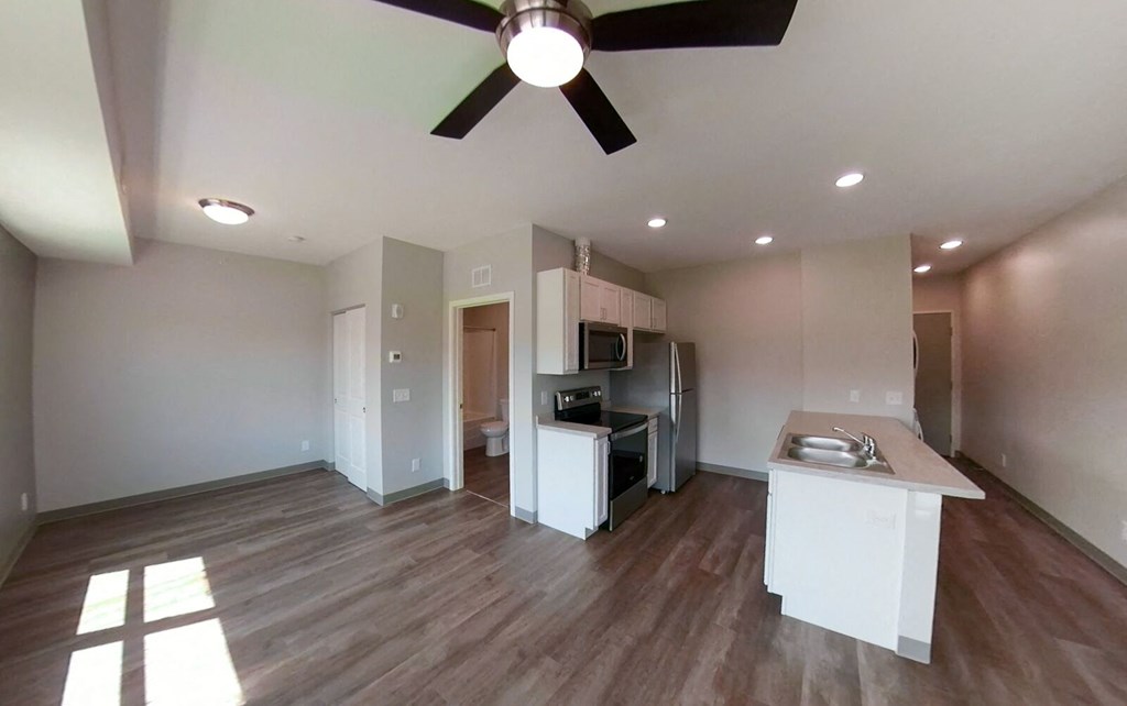 an empty living room with a kitchen and a ceiling fan