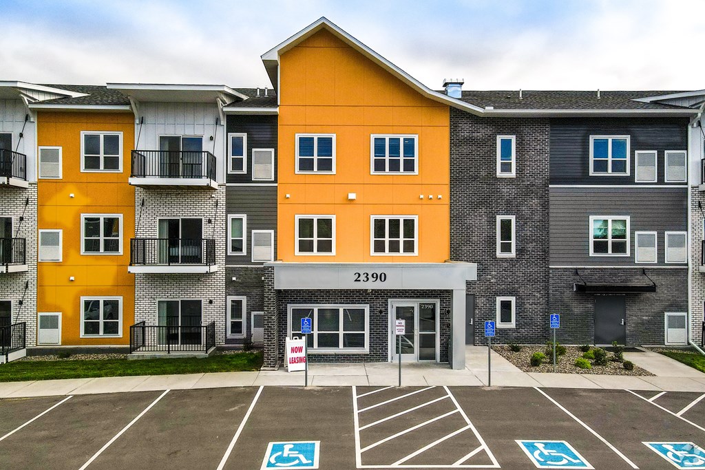 an apartment building with an orange and gray facade in a parking lot