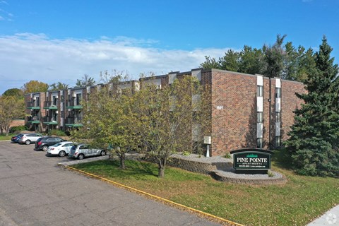 A parking lot in front of a brick building with a sign that says Pine Pointe.