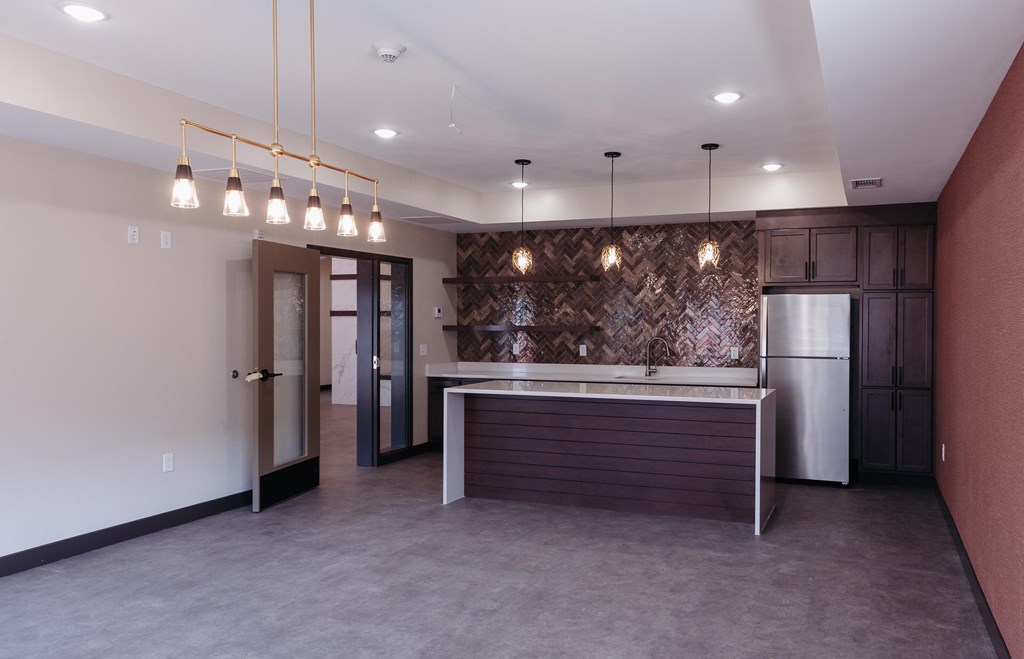 an empty living room with a kitchen and a refrigerator