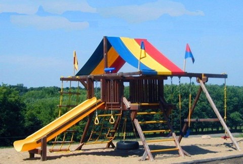 A playground with a yellow slide and a wooden structure with flags.