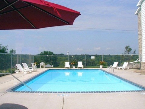 A red umbrella is shading a pool area with chairs.