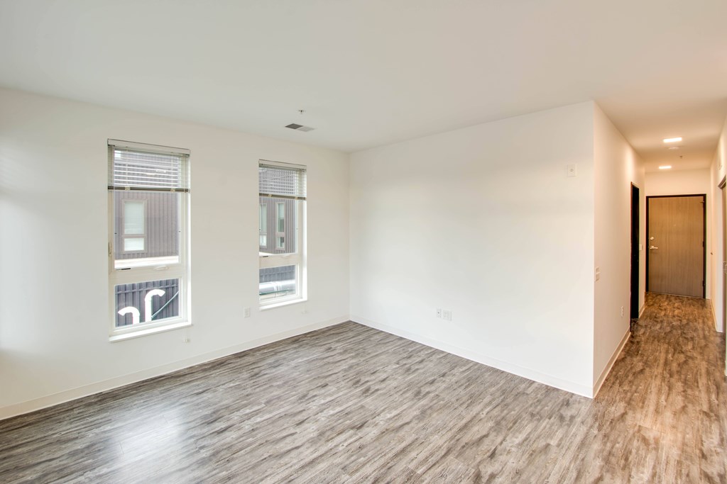 A room with wooden flooring and two windows.