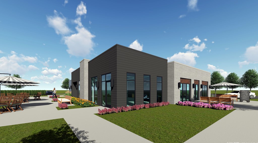 A modern building with a grey exterior and large windows is surrounded by a well-manicured lawn and outdoor seating area.