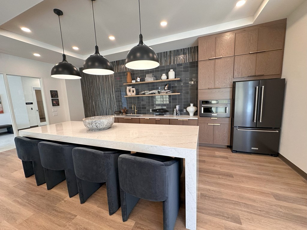A modern kitchen with a long island and dark chairs.