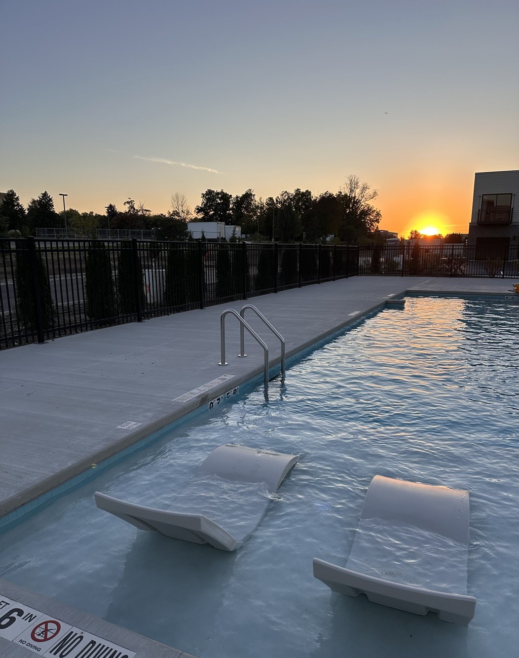 Two sun loungers are in a pool with a sunset in the background.