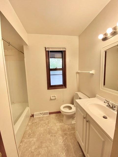A bathroom with a toilet, sink, and a window at Root River Apartments, Greendale, 53129