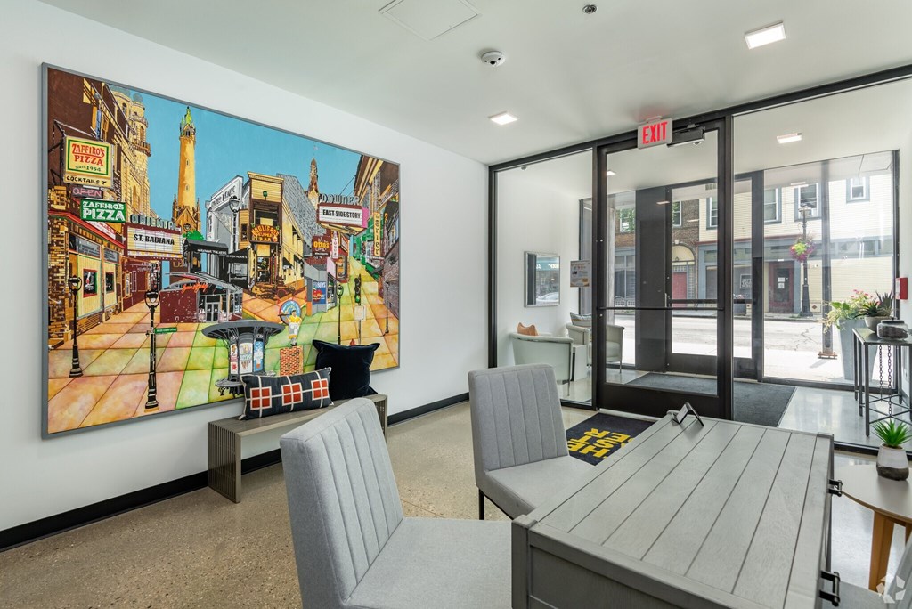 A large painting of a street scene is hanging on the wall in a room with a table and chairs.