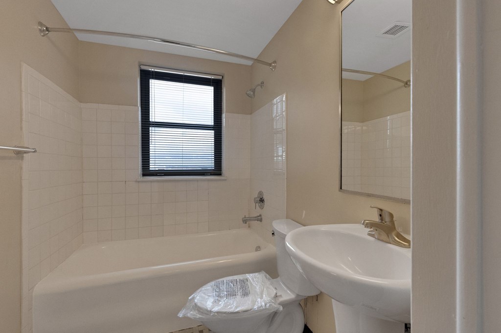 A white sink is in a bathroom with a white tub and a window.