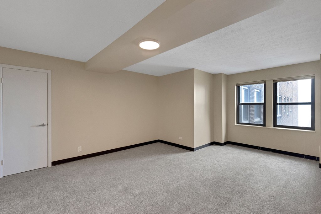 A room with a carpeted floor and a window with a view of a street.