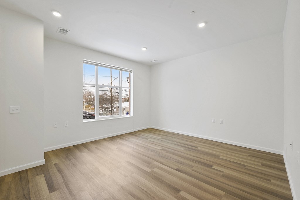 a living room with white walls and wooden floors and a window